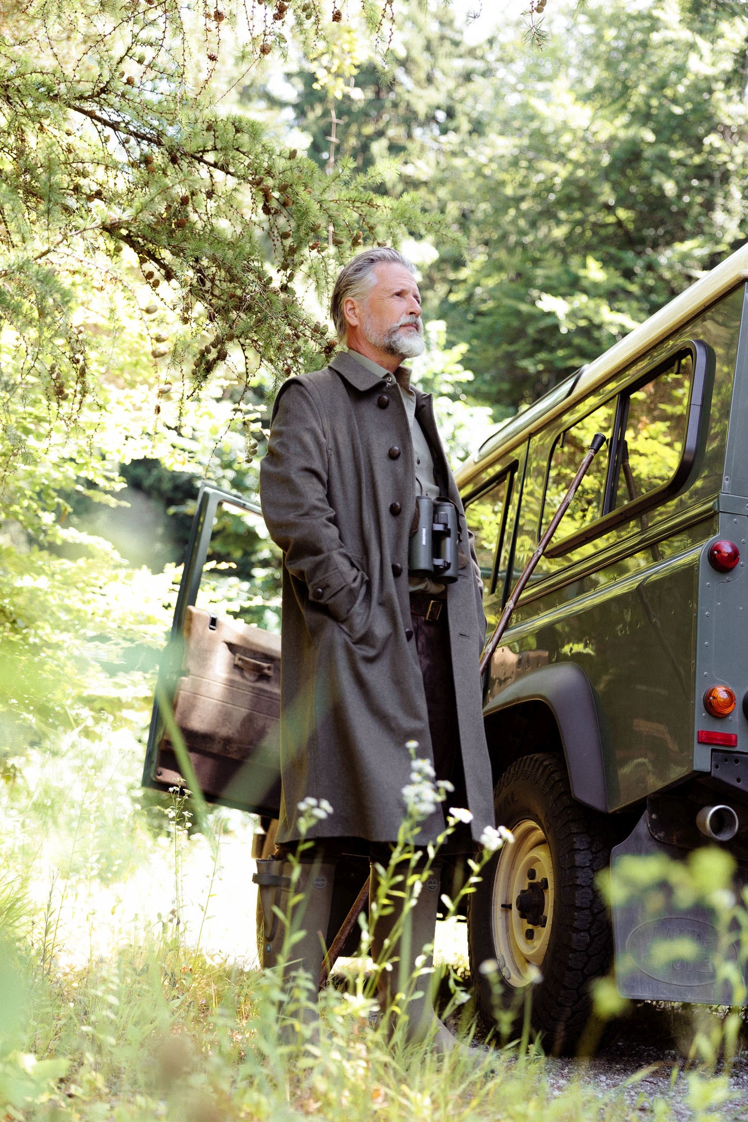 Außenaufnahme im Wald neben einem Auto, Habsburg Hubertusmantel in Cashmere, grün, halb geöffnet - Eleganter Jagdmantel für Herren, am Modell.